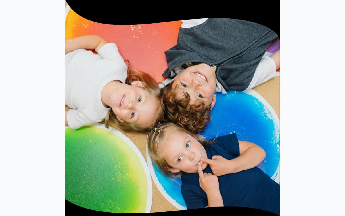 Three children smiling while exploring colorful sensory floor tiles in a playful learning environment