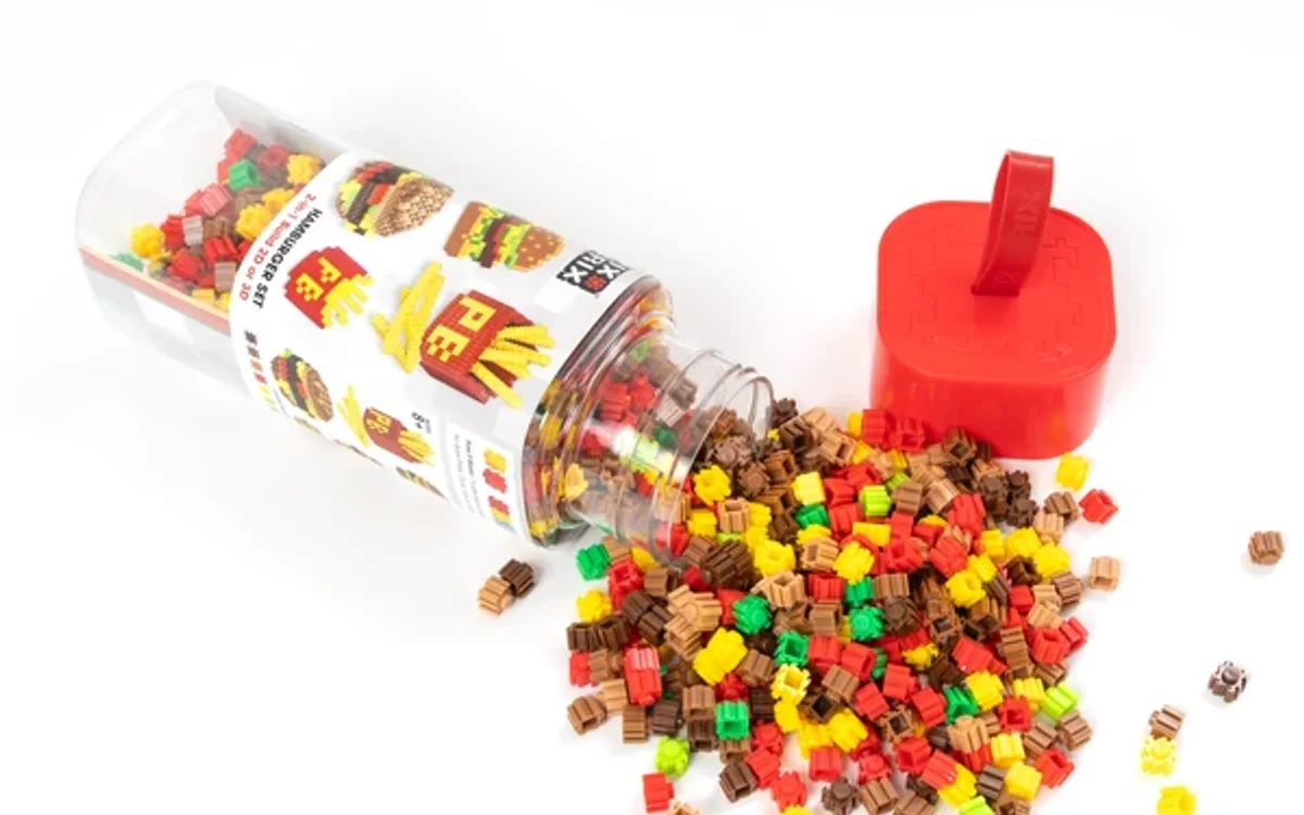 Colorful building block toys spilling out of a transparent container with a red lid on a white background.
